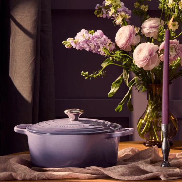 A cast iron cookware item on a table next to flowers in a vase and a candle