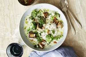 A bowl of rice topped with broccoli tofu cubes and a curry sauce served with garnishes