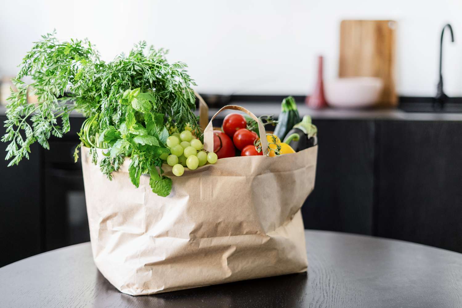 A grocery bag on a table containing fresh vegetables and fruits