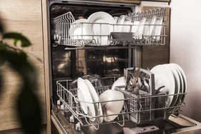 Open dishwasher with clean utensil inside, cutlery, glasses, dishes at kitchen