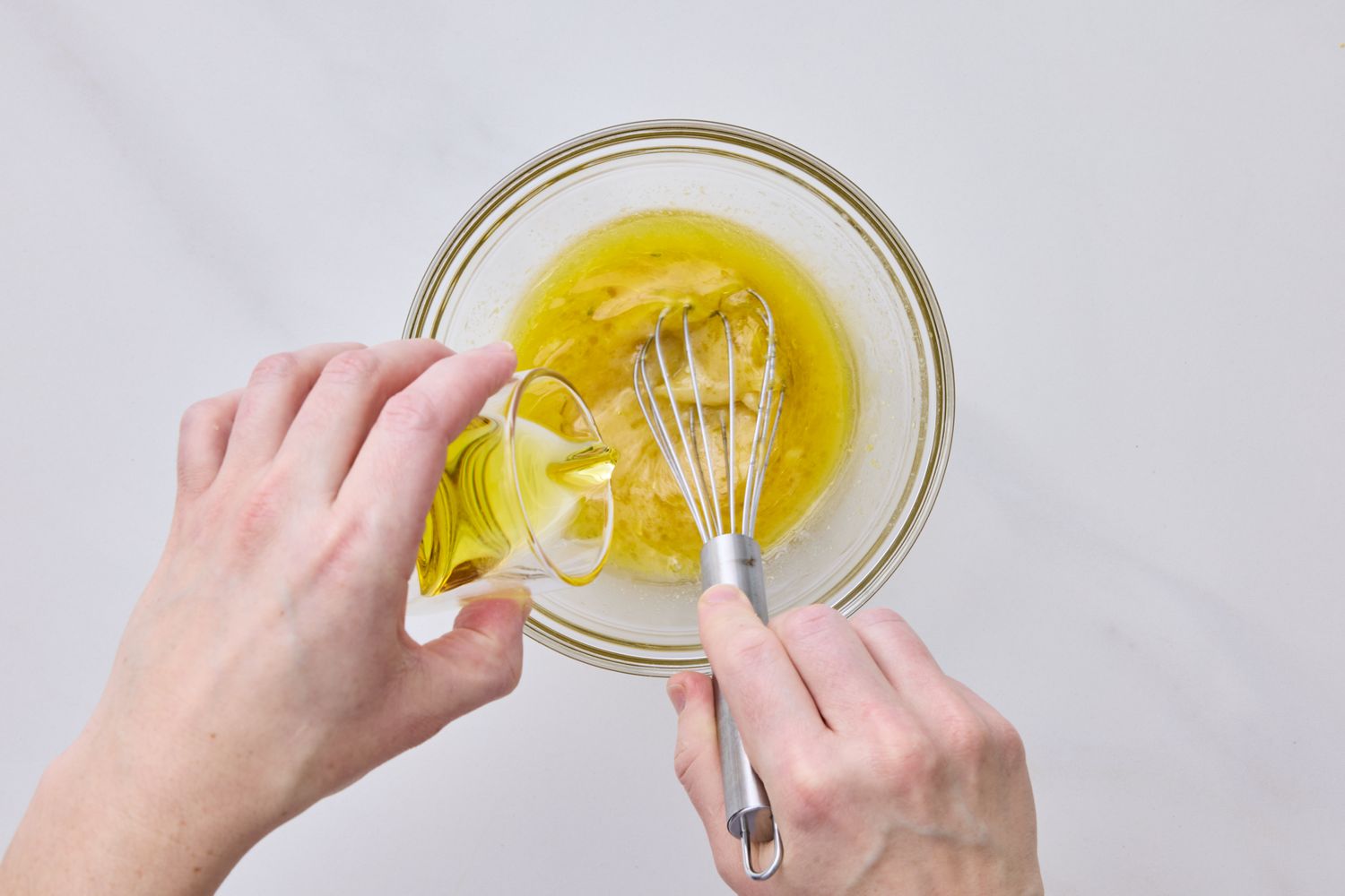Hands making salad dressing in a glass bowl with a whisk