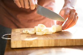 Someone cutting a banana on a wooden cutting board with a knife