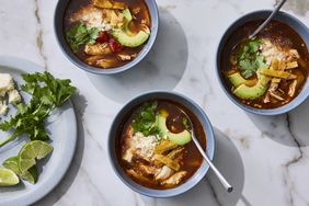Three bowls of Mexican chicken tortilla soup garnished with avocado cilantro and cheese with lime wedges and cheese on the side