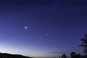 Night sky with celestial bodies and a crescent moon visible above a silhouette of treetops and hills