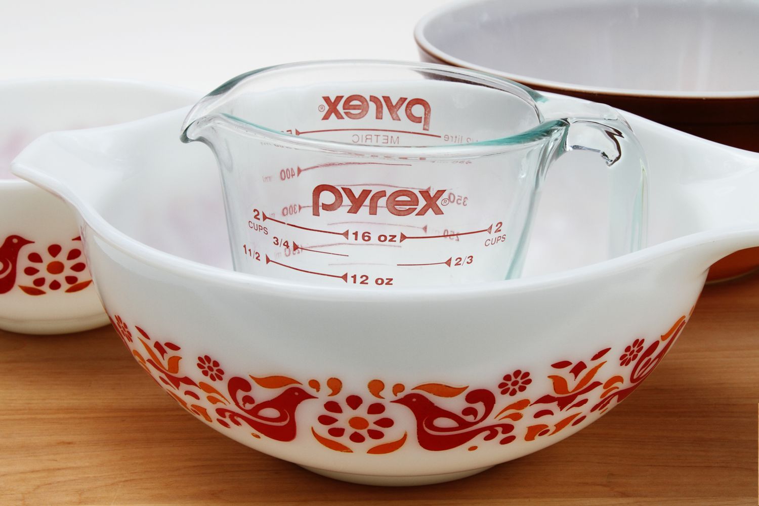 Stacked Pyrex mixing bowl with bird design and measuring cup on a wooden surface