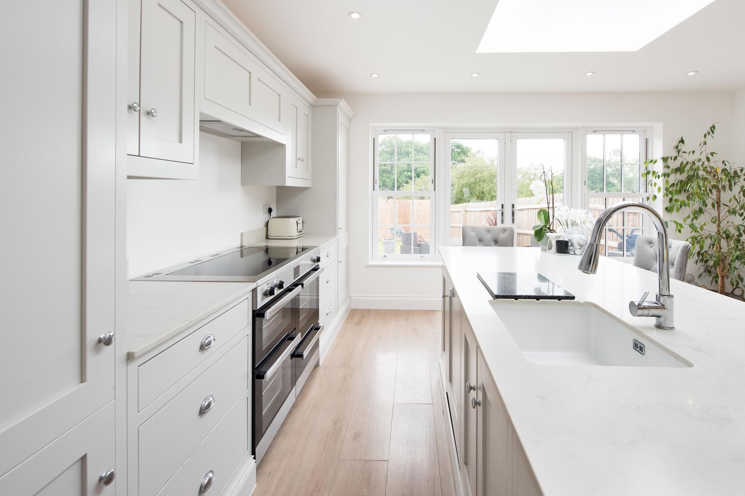 Modern kitchen with white cabinets a central island builtin appliances and large windows overlooking a backyard