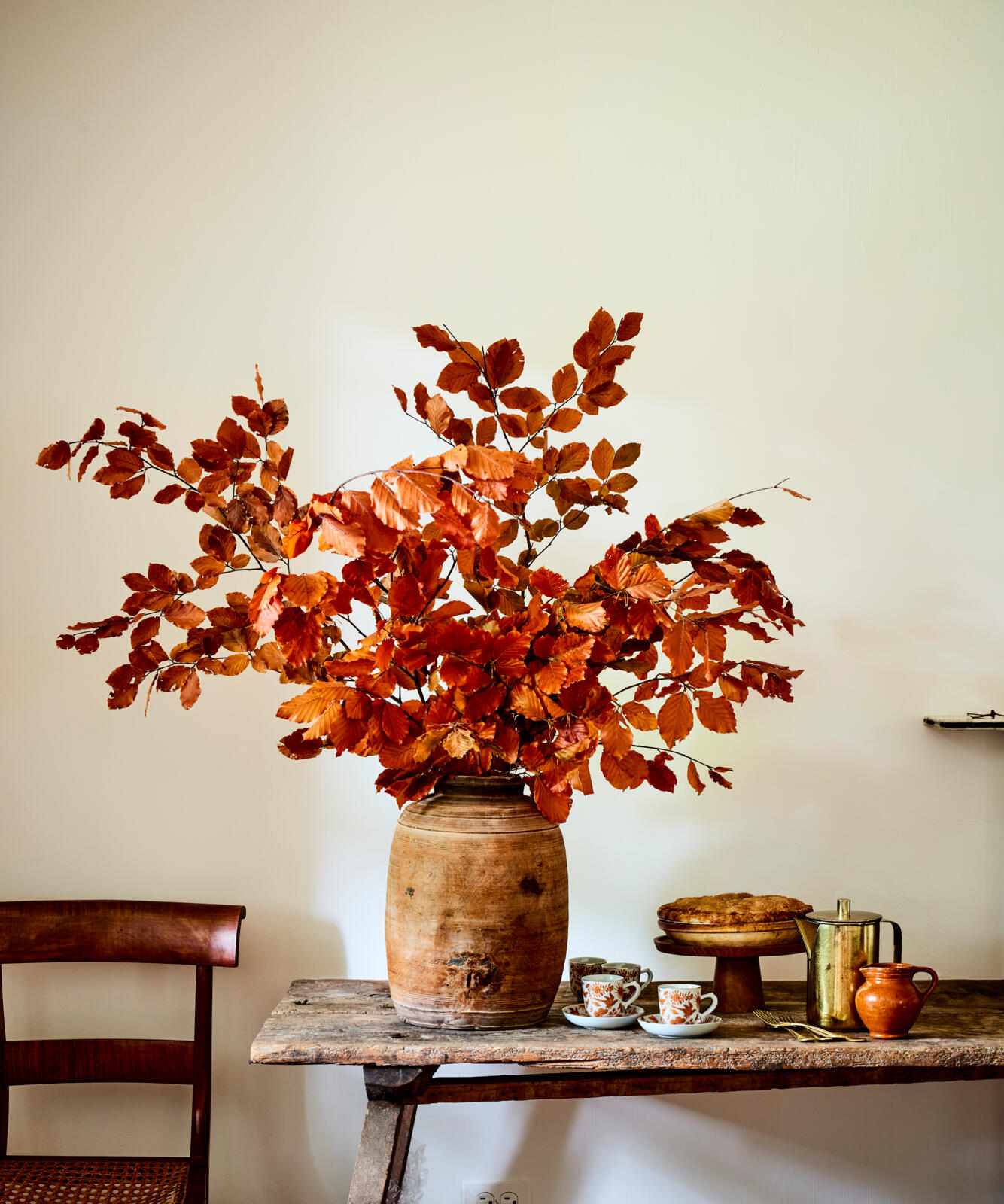 A sideboard with an arrangement of branches in a vase cups and small kitchenware items