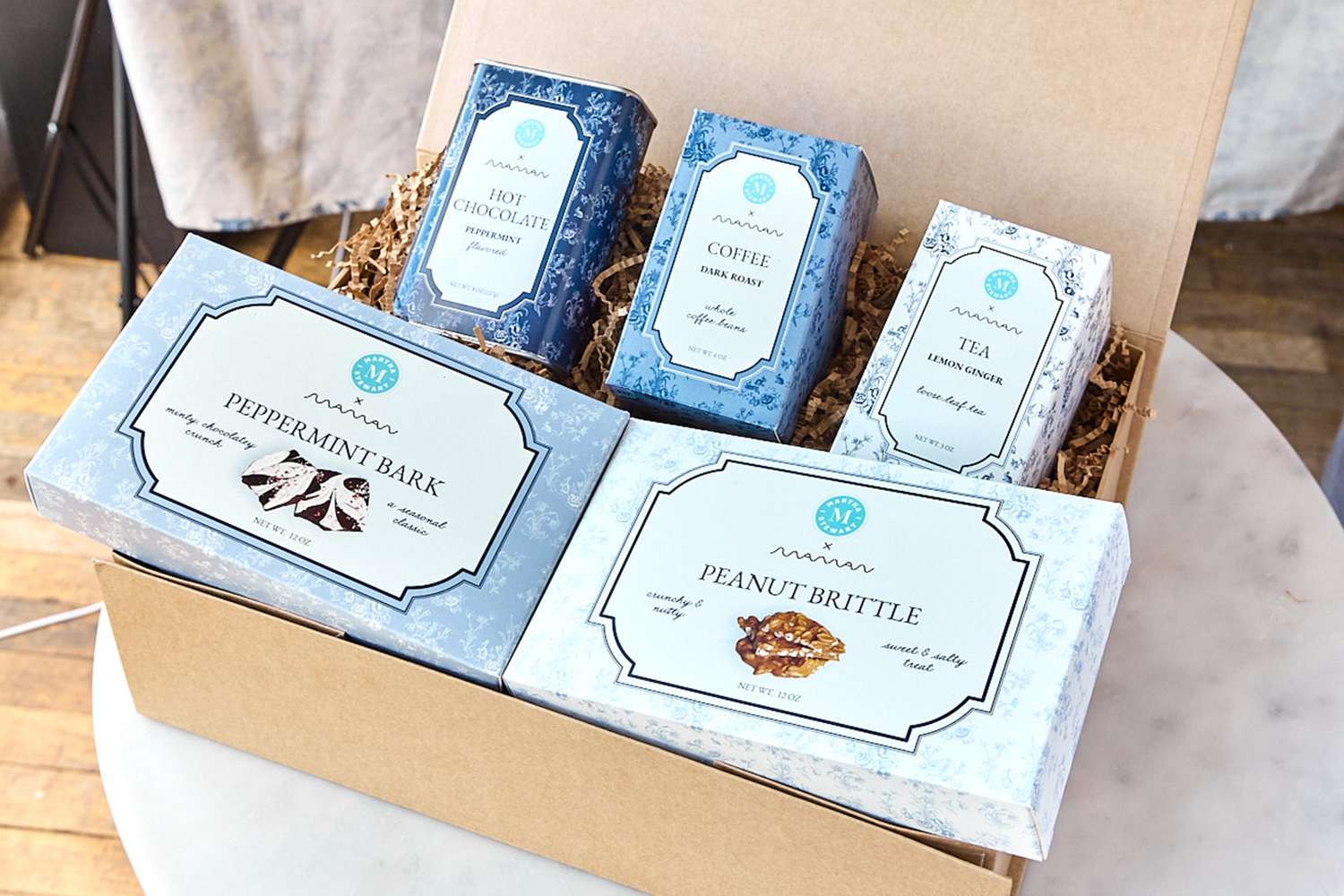 A boxed arrangement of gourmet food items including tea coffee peppermint bark and peanut brittle