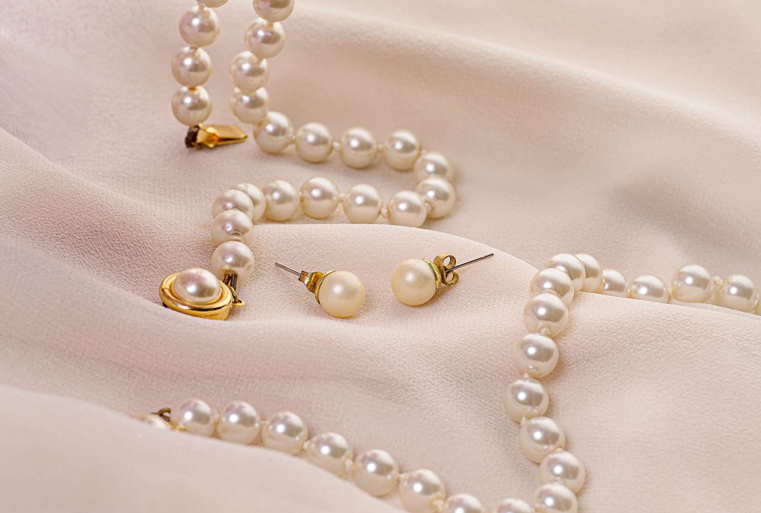 A set of pearl jewelry consisting of earrings and necklaces placed on a soft fabric background