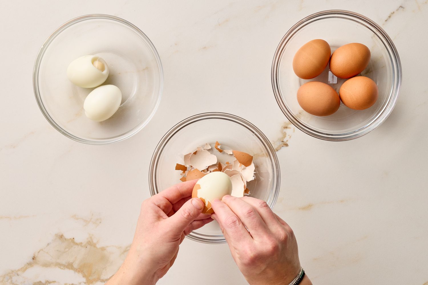 Person peeling a hardboiled egg with bowls of eggs and eggshells nearby