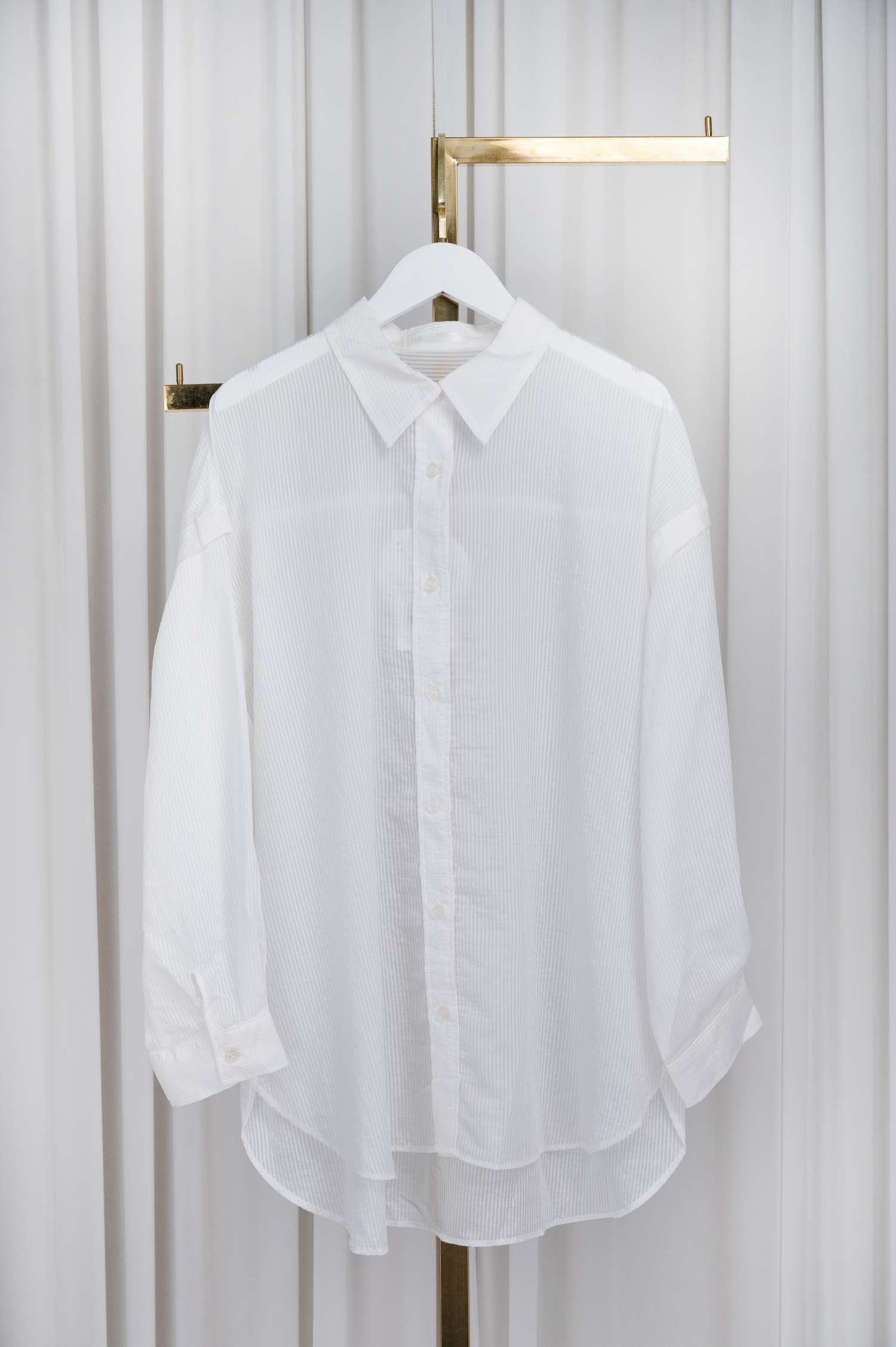 A longsleeved shirt hanging on a hanger displayed on a metallic stand