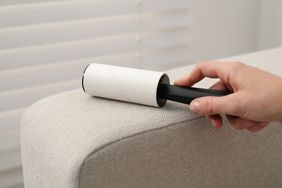 A hand using a lint roller on a couch armrest
