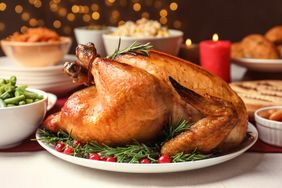 A roasted turkey served on a plate garnished with herbs and cranberries with side dishes and a red candle in the background