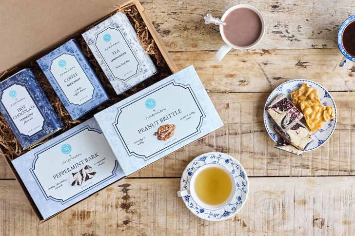 A collection of packaged treats and drinks displayed on a wooden table including tea chocolate and brittle