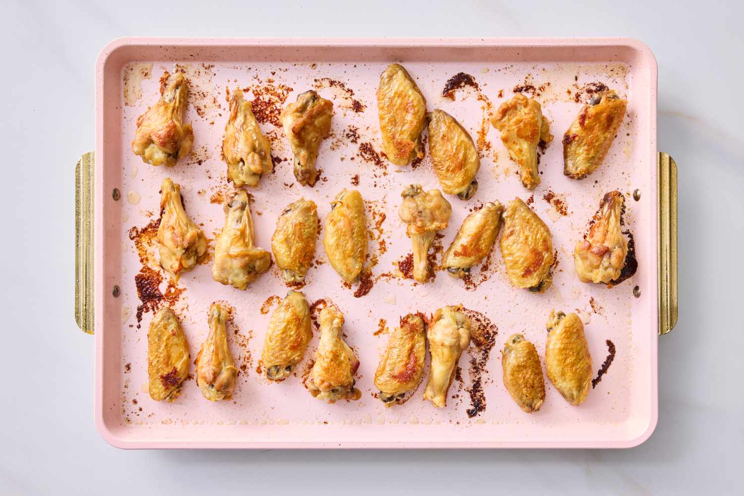 A baking tray with several baked chicken wings positioned in rows