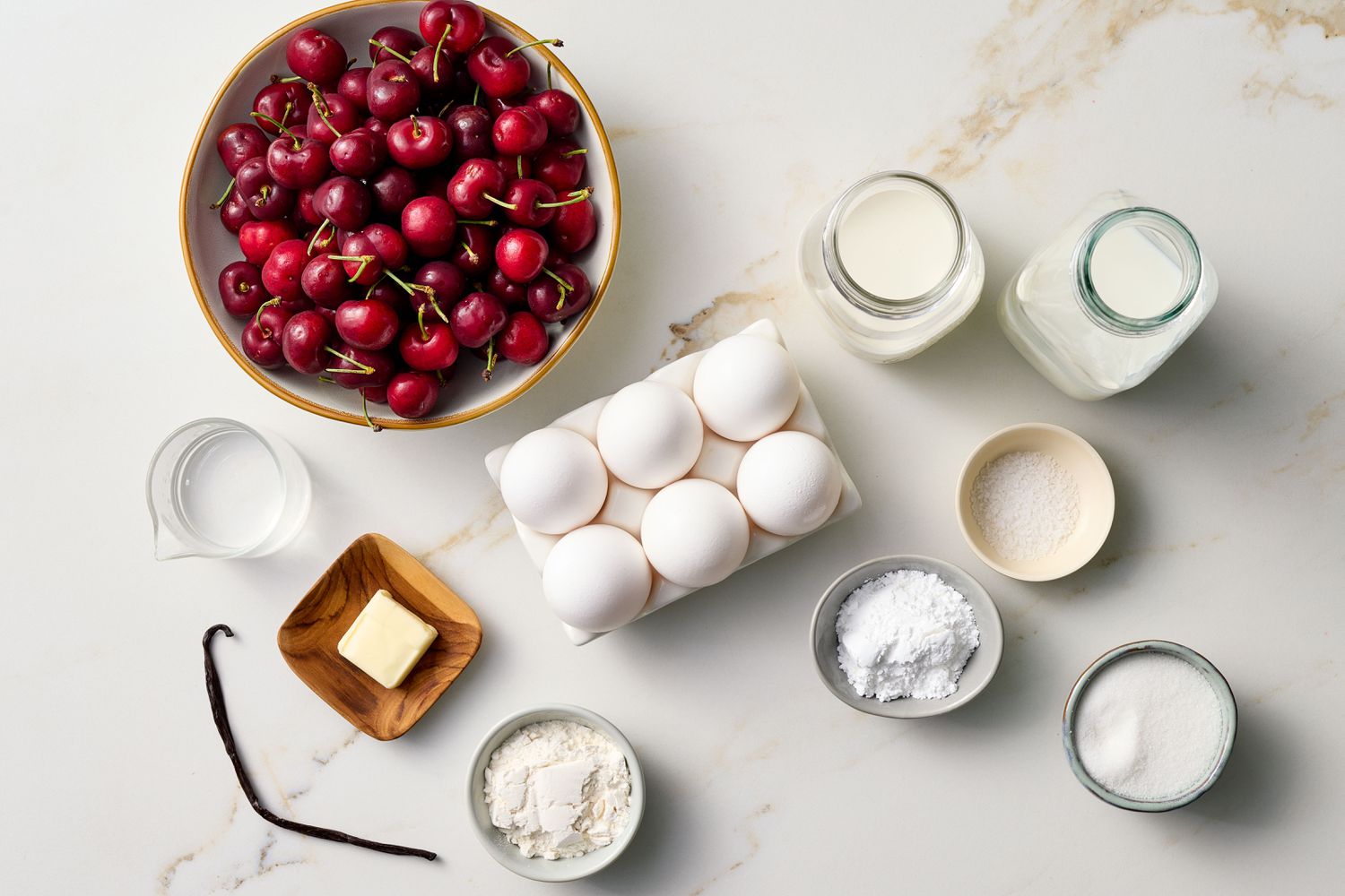 Ingredients arranged for cherry clafouti preparation, including fresh cherries, eggs, milk, sugar, and flour on a countertop