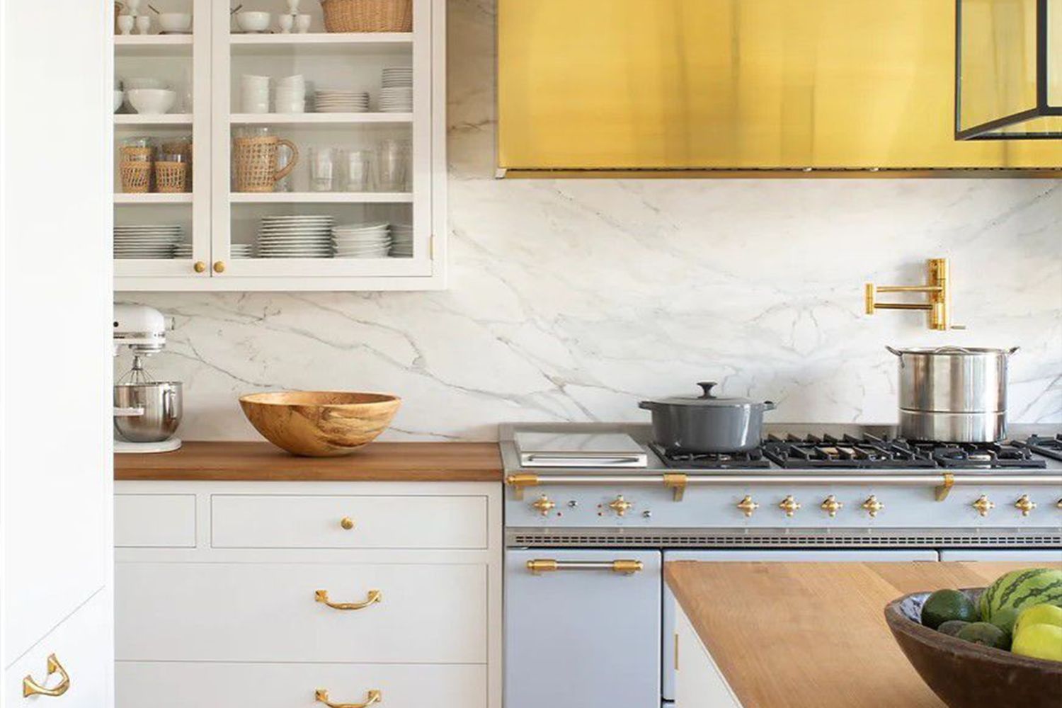 A kitchen featuring a marble backsplash a stove with a pot and wooden countertops with a fruit bowl