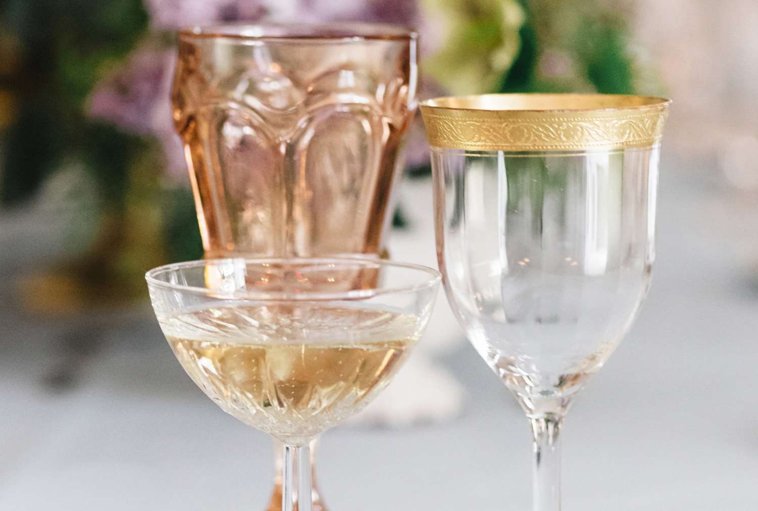 Various glasses arranged on a table including a wine glass with gold trim and a coupe glass with liquid