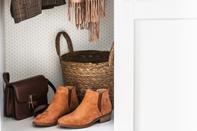A closet shelf displaying leather ankle boots a woven basket a brown handbag and hanging clothes items