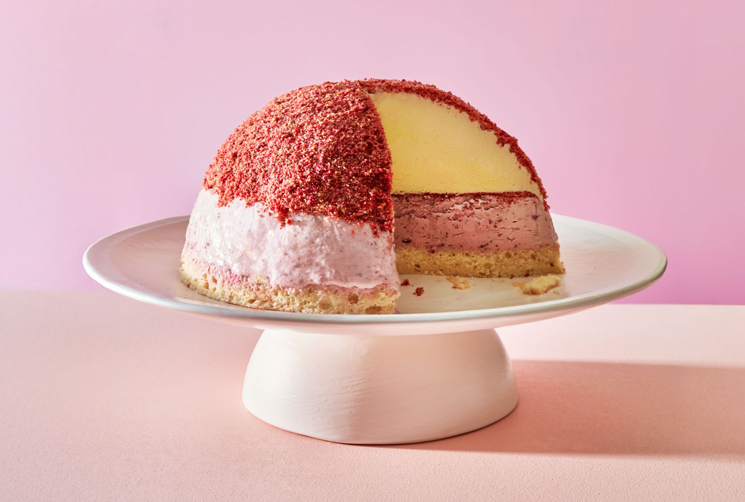 A cheesecake bombe dessert with sections of different filling exposed, displayed on a pedestal plate