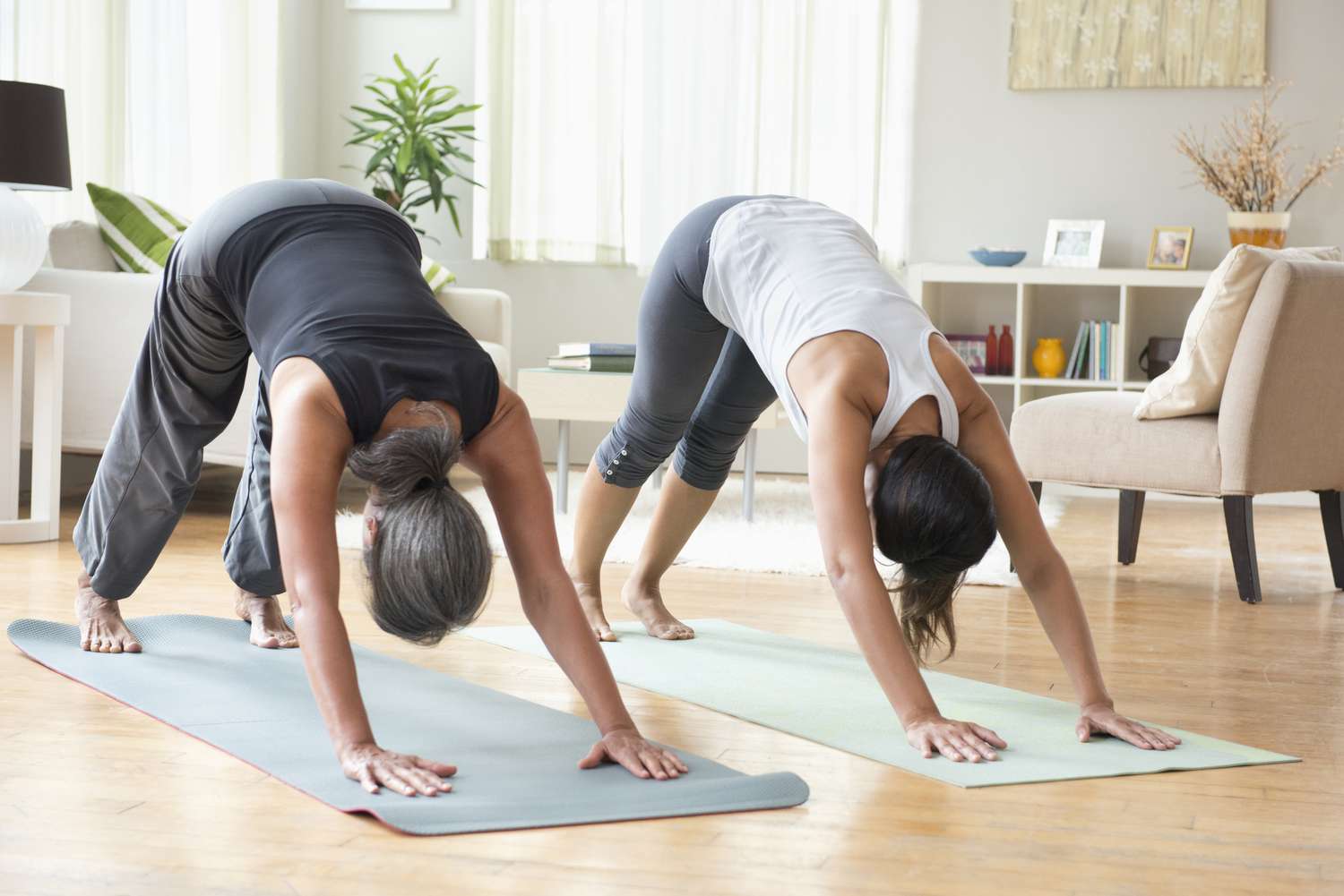 Two people practicing yoga in a living room performing a downwardfacing dog pose on yoga mats