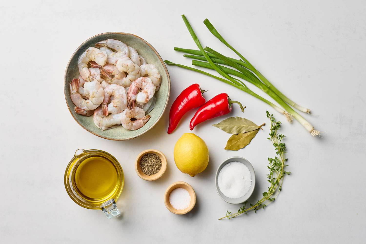 Ingredients including shrimp red chiles green onions lemon herb sprigs oil salt and other seasonings arranged on a surface