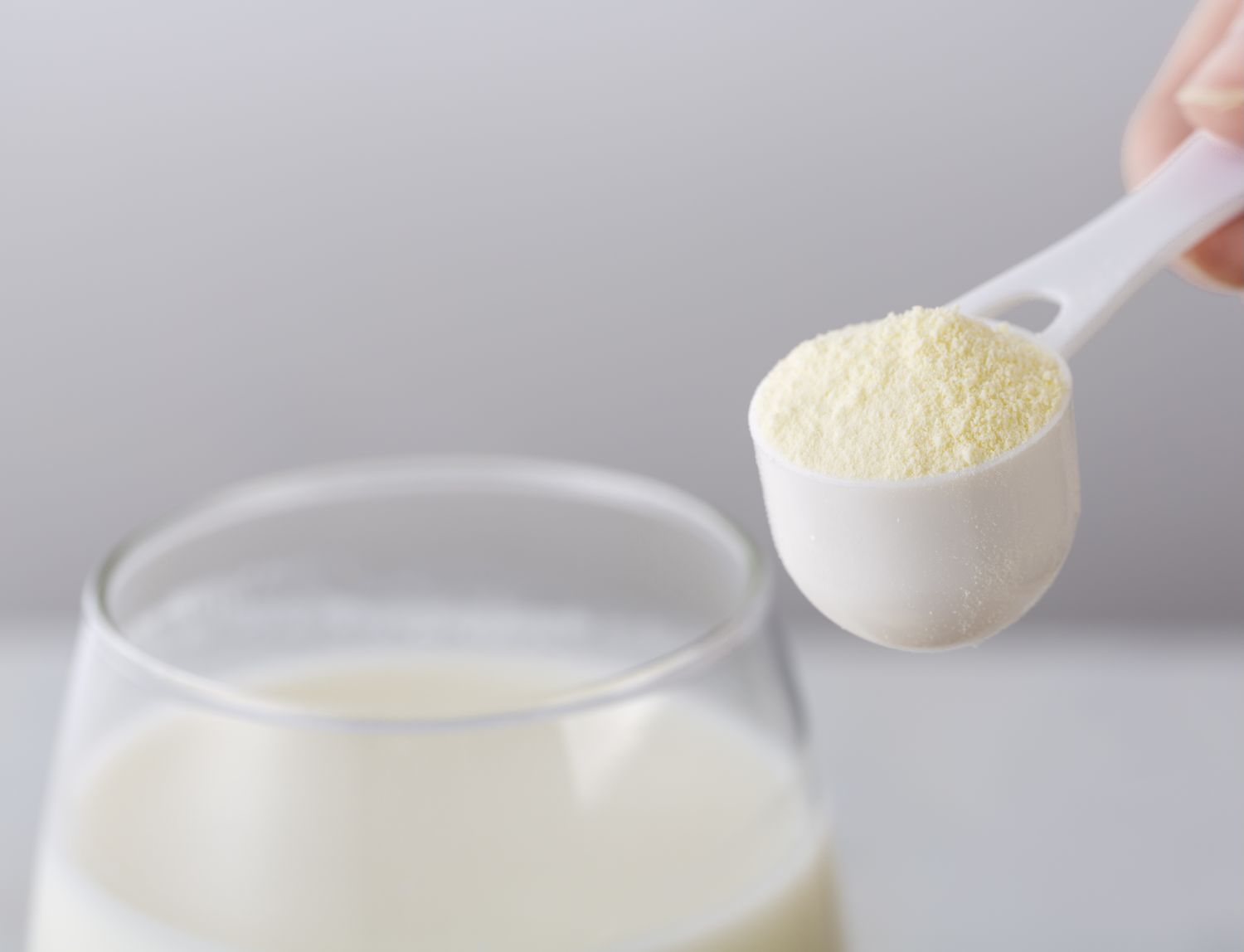 A measuring scoop of powdered supplement held above a glass of liquid