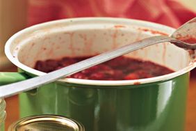 Jars of strawberry preserves next to a green pot filled with preserves with a ladle resting inside