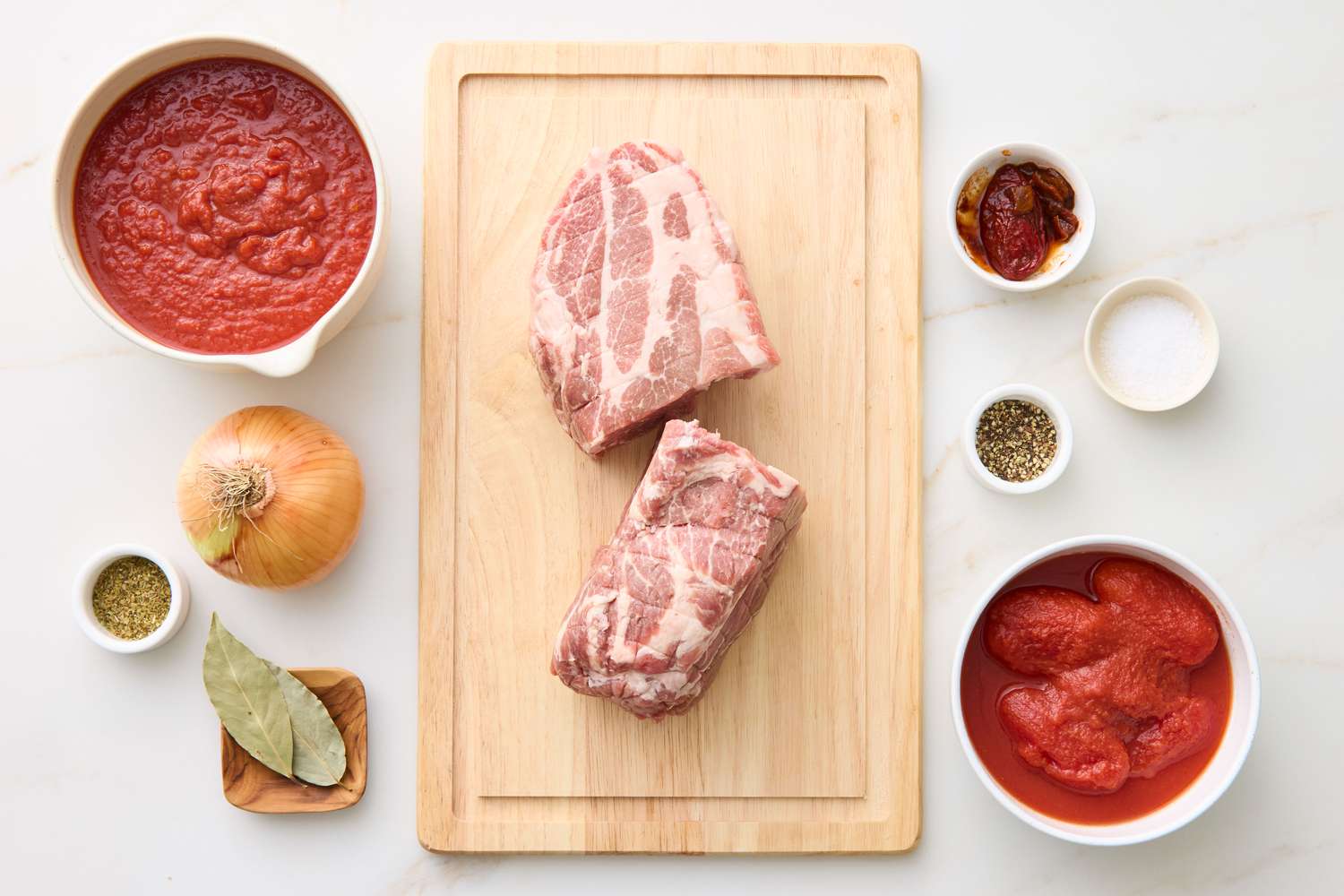 Ingredients for slow-cooker pulled pork arranged on a surface, including raw pork on a cutting board, tomatoes, onion, and spices