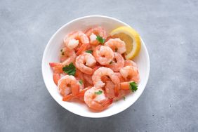 A bowl of cooked shrimp garnished with parsley and a lemon wedge