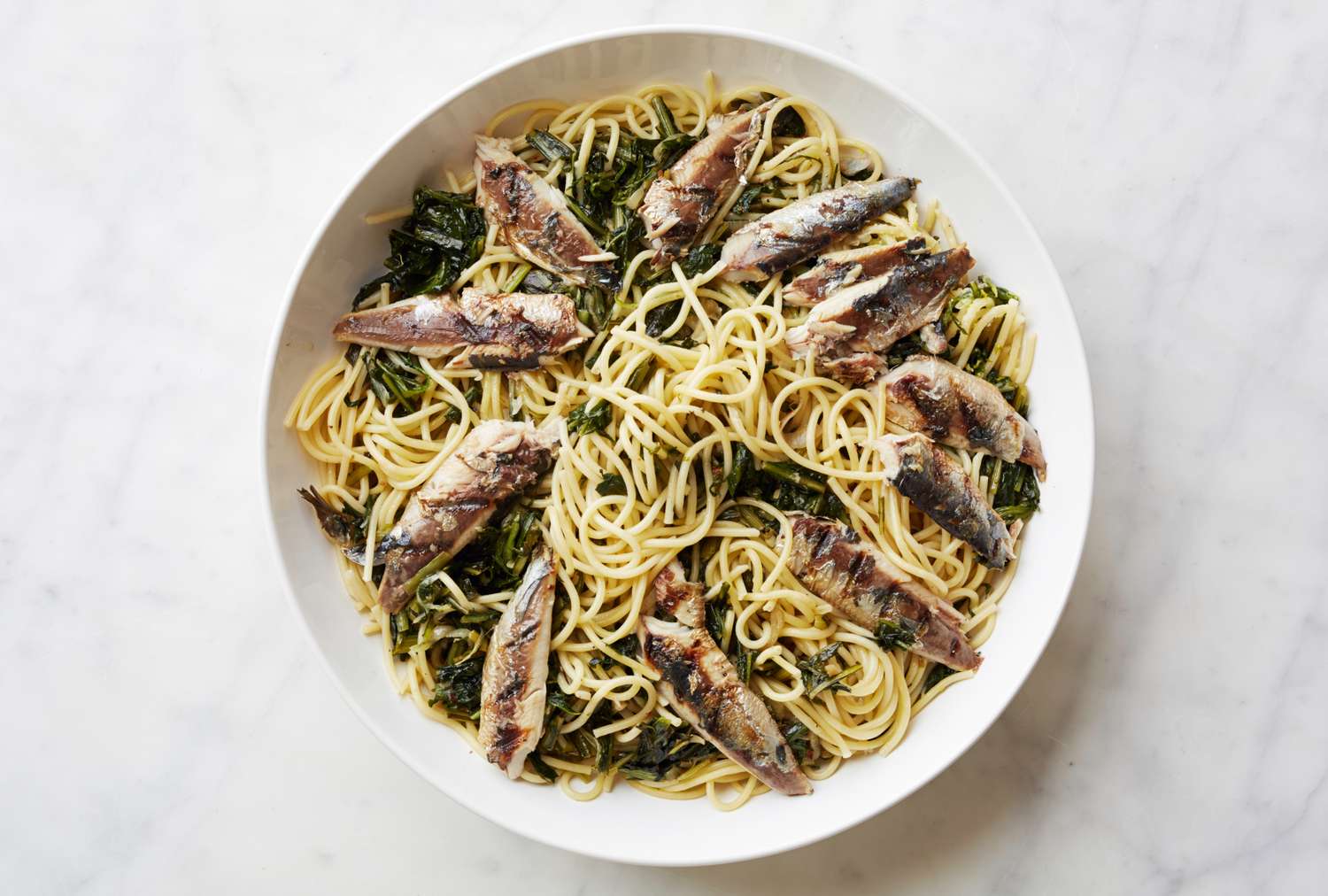 A plate of pasta topped with sardines and sauted greens highlighting a seafood pasta dish