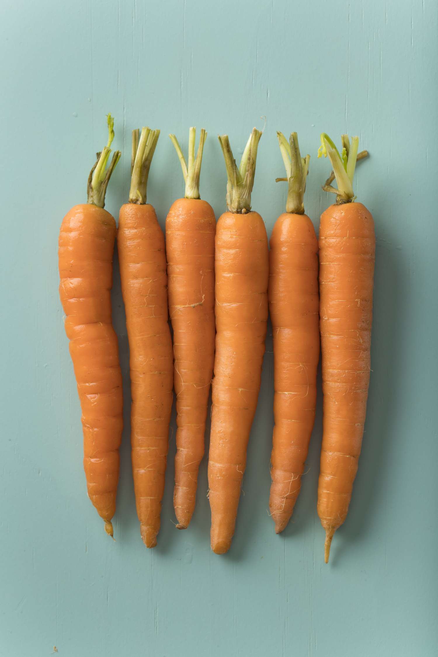 orange carrots with tops cut off on blue-green surface
