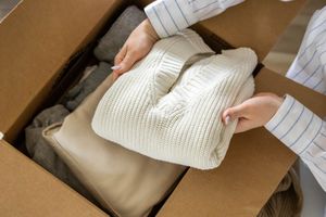 A person placing clothing items including a sweater into a cardboard box symbolizing a donation or packing activity