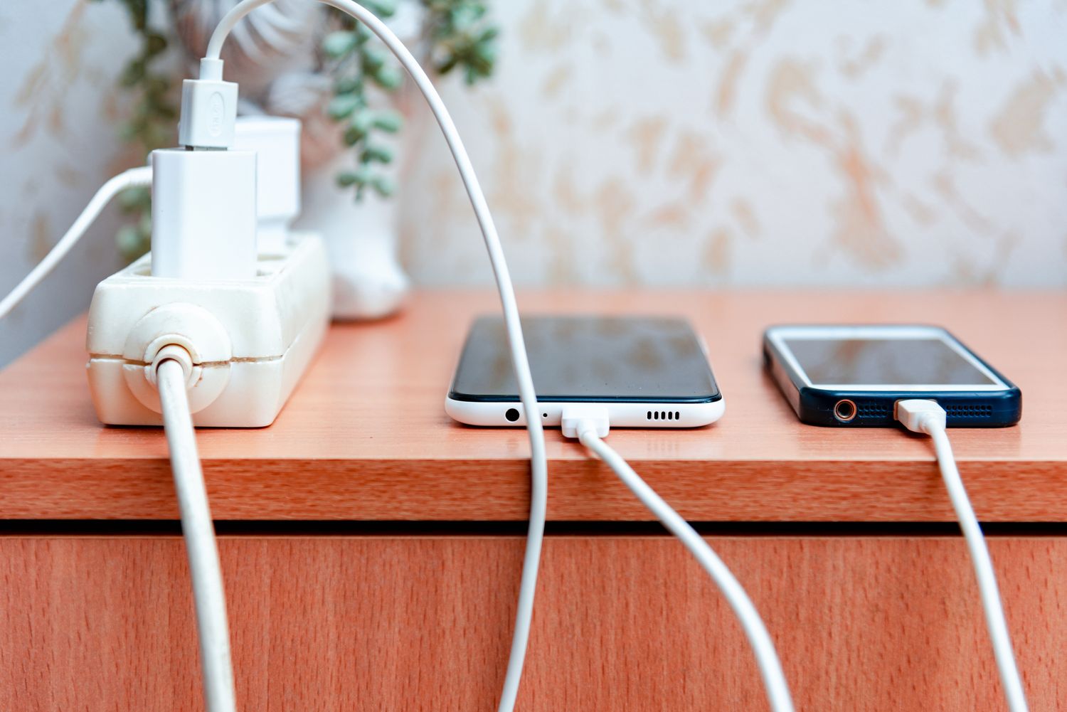 Two smartphones charging on a wooden surface connected to a power strip
