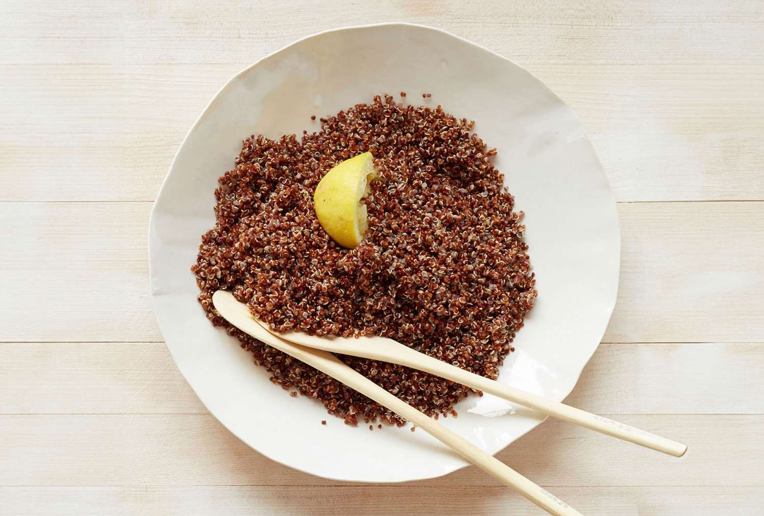 A plate of cooked red quinoa garnished with a lemon wedge and accompanied by two wooden utensils