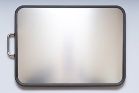 A stainless steel cutting board with a handle on the left