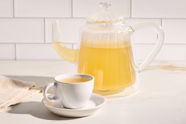 A glass teapot with ginger tea next to a cup on a saucer