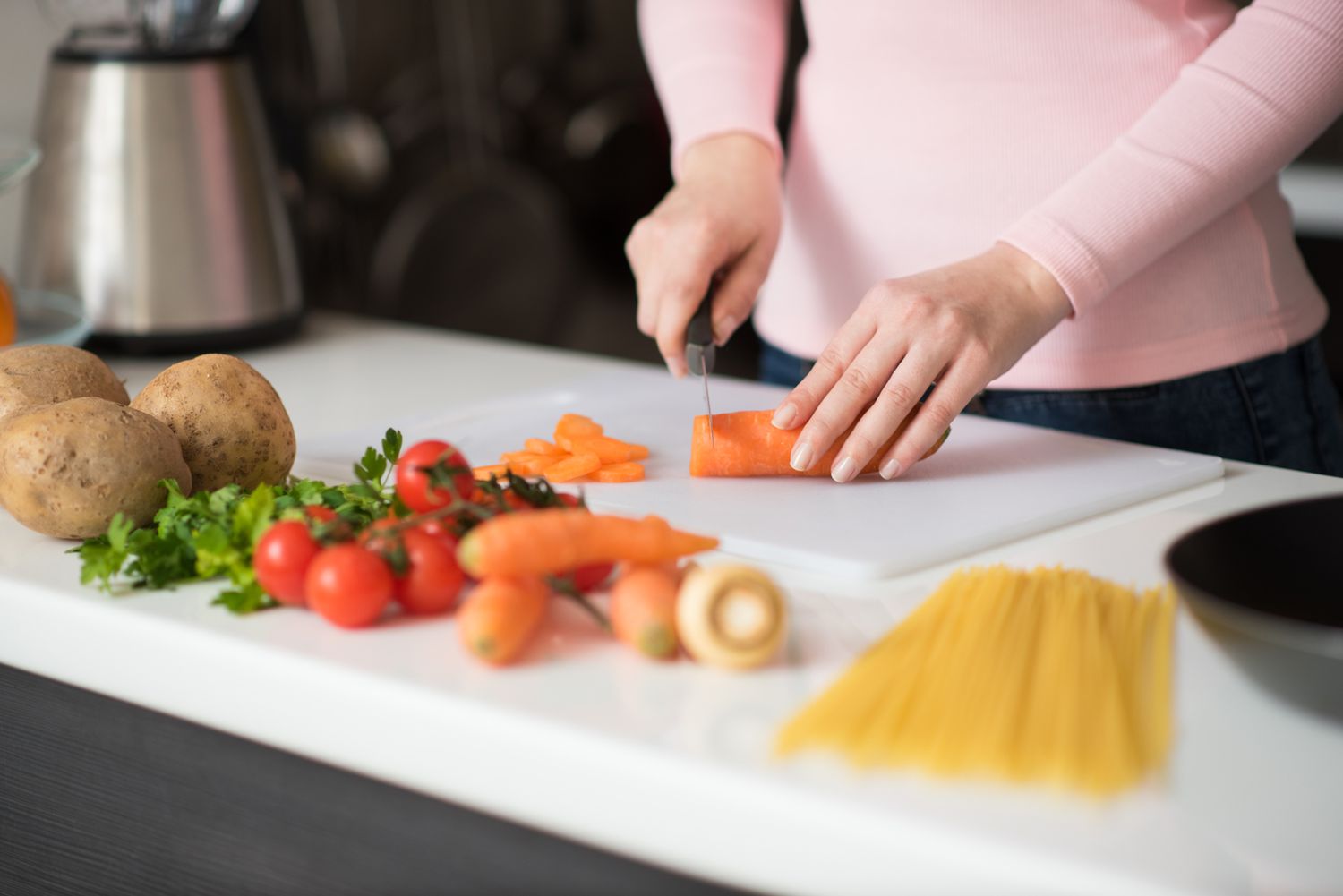 person chopping carrot on cutting board next to various other foods