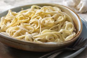 A bowl of fettuccine pasta with garlic clove in the background