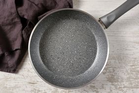A nonstick frying pan with a speckled surface placed on a wooden surface next to a fabric cloth