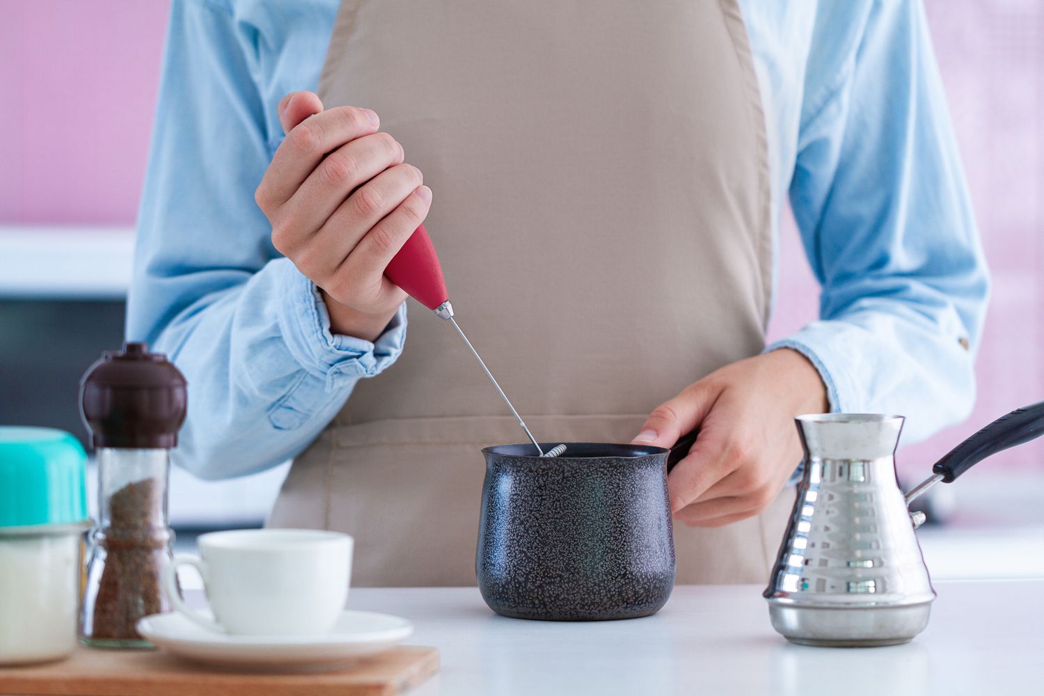 woman using a milk frother in a black ceramic vessel