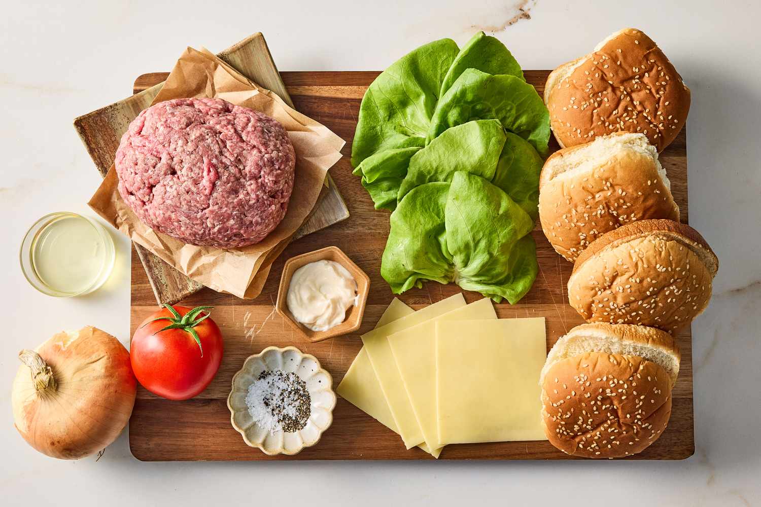 Ingredients for making burgers on a wooden board including lettuce burgers buns cheese ground meat and condiments