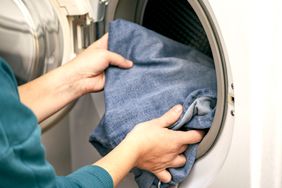 Hands placing denim fabric into a front-loading washing machine