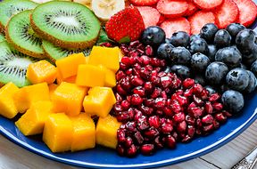 A platter of assorted fruits including kiwi strawberries mango cubes pomegranate seeds and blueberries arranged in sections