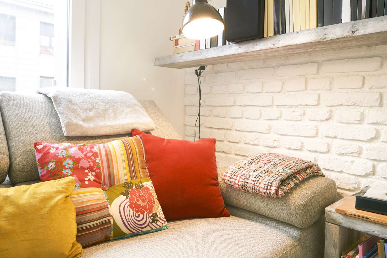 A cozy living area with a sofa adorned with colorful cushions a lamp on the wall shelf and a plaid blanket nearby
