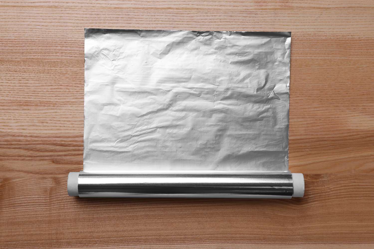 A roll of aluminum foil partially unrolled on a wooden surface