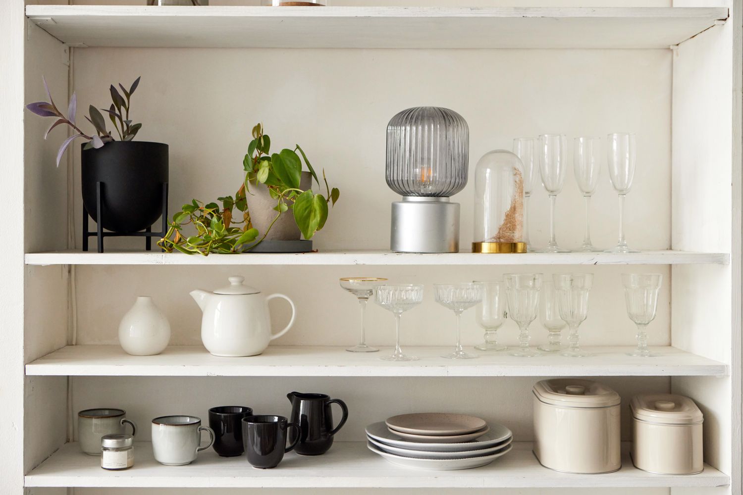 Modern white shelving unit displays a variety of homeware items, including plants, crockery, glassware, and decorative objects, creating a stylish and organized space in a contemporary home
