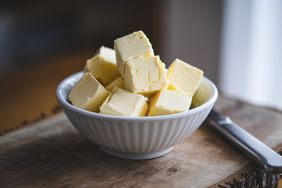 A bowl filled with cubes of butter on a wooden surface with a butter knife nearby