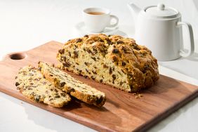 A loaf of Irish soda bread with slices cut placed on a wooden cutting board next to a cup of tea and a teapot