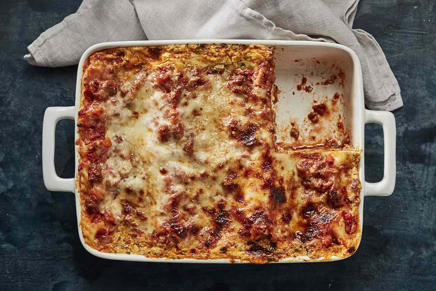 A rectangular lasagna dish with a single portion served resting on a cloth